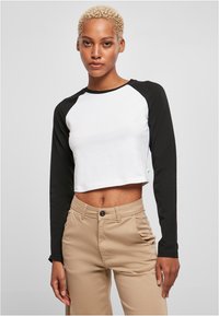 Crop top med hvid krop og sorte lange ærmer. Blødt bomuldsstof; rund halsudskæring; minimalistisk design. Båret med beige bukser.