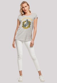 Grå t-skjorte med korte ermer som har Hufflepuff-emblemet i gult og svart. Kombinert med hvite skinny jeans og hvite sneakers.
