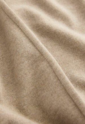Beiger Wollstoff mit einer sanften, strukturierten Oberfläche, die subtile Farbtonvariationen aufweist, sowie einer diagonal über das Bild verlaufenden Naht.