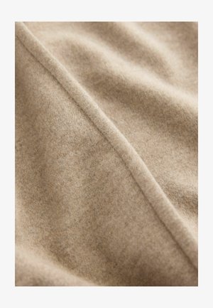 Beige villakangas, jossa on pehmeä ja tekstuuriin perustuva pinta. Näkyvissä on hienovaraisia sävyvaihteluita ja diagonaalinen sauma, joka kulkee läpi kuvan.