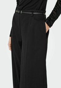 Czarne spodnie o dopasowanym kroju, gładka tekstura, z bocznymi kieszeniami i wąskim czarnym paskiem. Miękka, zwiewna tkanina zwiększa komfort.