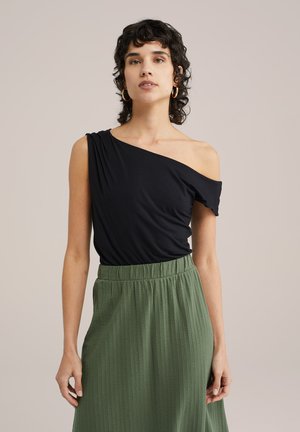 Schwarzes, ein-schultriges Top aus glattem Stoff, kombiniert mit einem grünen, strukturierten Rock mit elastischem Bund. Einfaches, lässiges Design.
