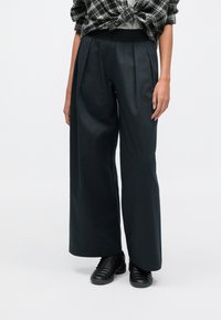 Calças pretas de perna larga feitas de um material liso, com um corte descontraído, pregas na frente e cintura elástica.