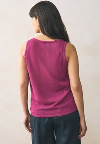 Top senza maniche fucsia con scollo rotondo, texture morbida e dettagli di orlo grezzo, abbinato a pantaloni scuri, visto da dietro.