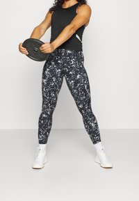 Svart atletisk linne i kombination med mönstrade, figurnära leggings i nyanser av svart och grått. Personen håller en viktskiva. Vita löparskor.