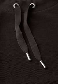 Schwarze Kapuzenjacke mit flachen, schwarzen Kordeln mit metallischen Spitzen vor einem strukturierten Stoffhintergrund. Klare Ösenbeschläge sichtbar.