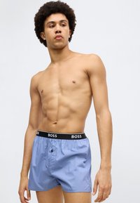Lyseblå boxershorts med en svart elastisk midjebånd som har merket "BOSS" i hvite bokstaver og en knappelukking foran.