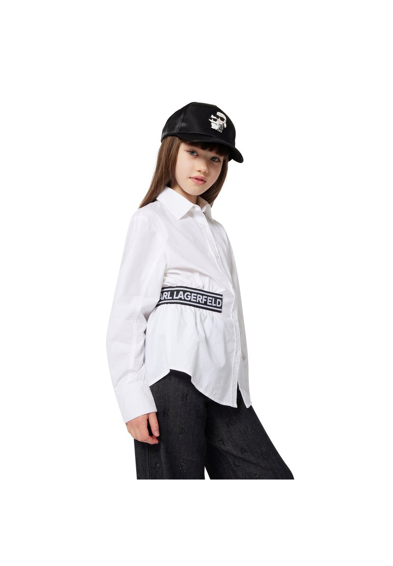 Camisa branca com bainha curva, com uma faixa elástica preta com o logótipo "KARL LAGERFELD". Boné preto com detalhe gráfico de caveira.