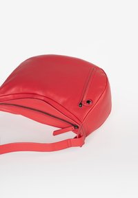 Borsa in pelle rossa con forma curva, manico singolo e chiusura con zip superiore. Tasche frontale con zip ben visibile e dettagli di cucitura minimi.