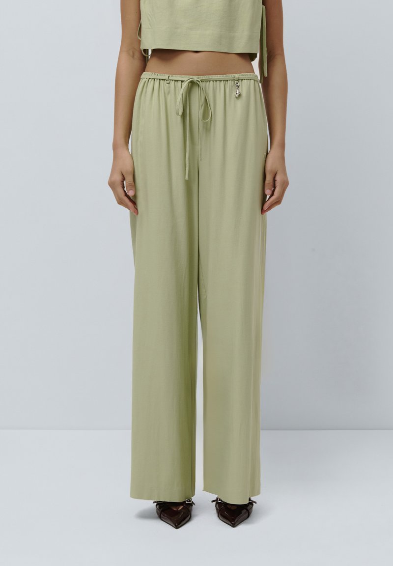 Pantaloni ampi di color verde chiaro, realizzati in un tessuto morbido con cintura elastica e cordoncino, dotati di una piccola accentuazione metallica.