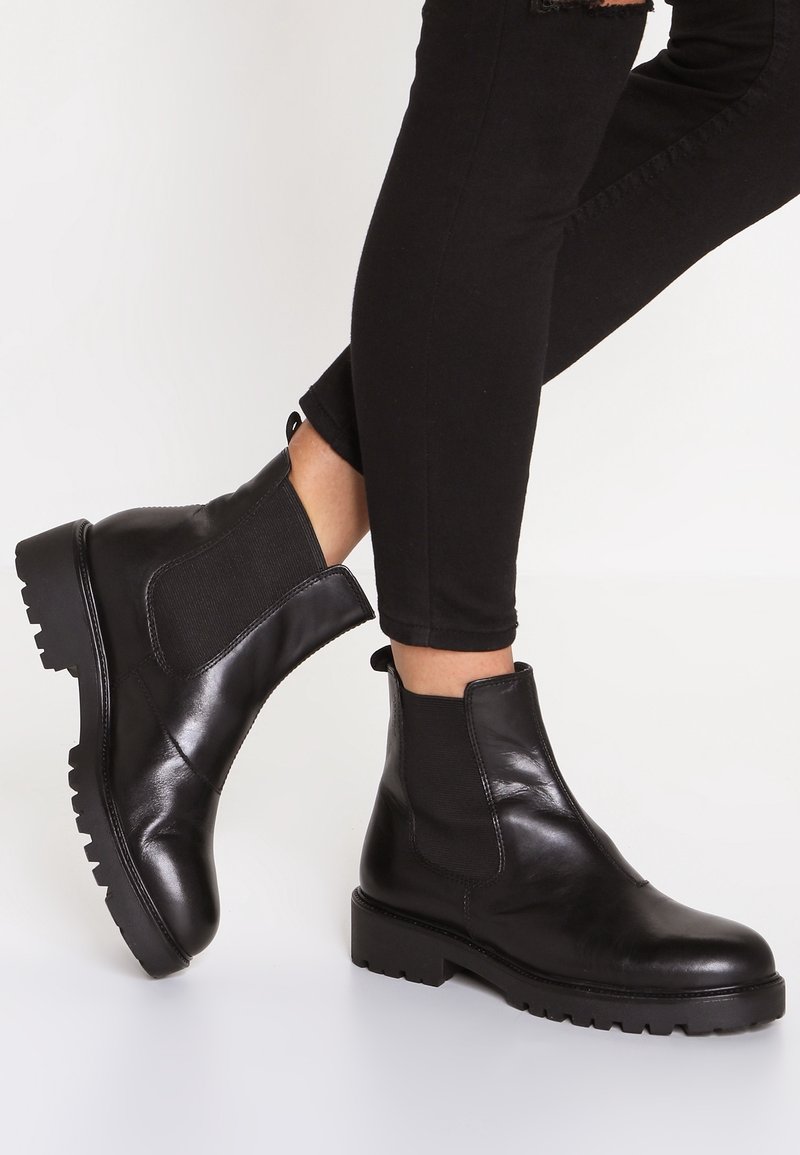 Bottes Chelsea en cuir noir avec semelle en caoutchouc, panneaux latéraux élastiques et bande de tirage au niveau du talon. Texture lisse et design à bout arrondi.