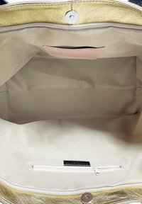 Kultainen ulkotasku, jossa on sileä pinta, sisältää beige sisävuoren ja vetoketjullisen taskun. Magneettinen napitus ylhäällä.