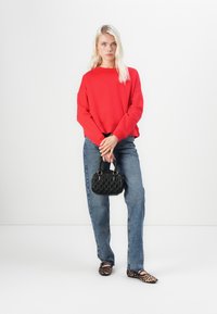 Sudadera roja de gran tamaño, jeans de mezclilla azul claro, bolso negro texturizado y zapatos planos de estampado de leopardo. Diseño simple y ajuste relajado.