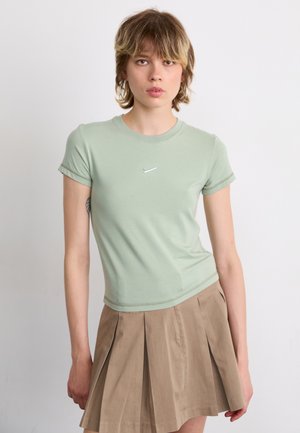 Light green fitted t-shirt made of soft fabric, short sleeves, featuring a small silver Nike logo on the chest, paired with a pleated beige skirt.