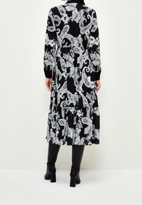 Vestido negro con un patrón de paisley blanco, mangas largas, dobladillo en capas y tejido texturizado. Combinado con botas negras hasta la rodilla.