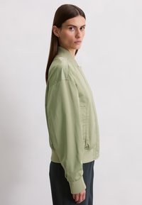 Light green bomber jacket with a ribbed collar and cuffs, featuring a smooth, shiny texture and side pockets.
