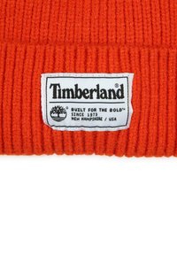 Tissu tricoté côtelé orange avec une étiquette rectangulaire blanche Timberland affichant le logo et le texte "Conçu pour les audacieux, depuis 1973, New Hampshire, États-Unis."
