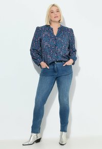 Blusa de manga larga con patrón en azul oscuro y acentos en rosa y verde, combinada con pantalones ajustados azul oscuro y botas metálicas plateadas hasta el tobillo.