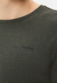 T-shirt corto a maniche corte di un verde scuro, con una texture, colletto a girocollo e un sottile logo VAUDE in rilievo sul petto. Tessuto morbido, design casual.