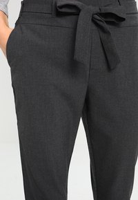 Calças cinzas escuras com uma textura suave, apresentando um laço de tecido na cintura, bolsos laterais e um corte ajustado.