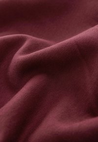 Bordeaux-stof har en blød, glat tekstur med et let ribbet mønster. Materialet virker let og fleksibelt.