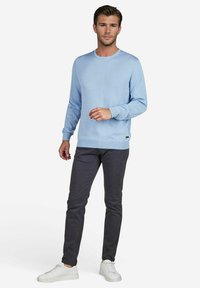 Helles blaues Strickpullover mit rundem Hals, langen Ärmeln und gerippten Bündchen, kombiniert mit dunkelgrauen Slim-Fit-Hosen und weißen Turnschuhen.