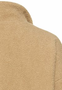Beige fleece stof med en blød, tekstureret overflade, forsynet med en afrundet krave og uden synlige lukninger.