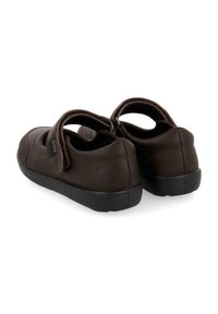 Zapatos de cuero marrón con punta redonda, talón acolchado y correa ajustable. Presentan una suela de goma negra texturizada y detalles de costura sutil.