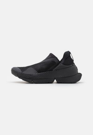 Crne slip-on cipele s prozračnom mrežastom gornjom površinom, teksturiranim gumiranim potplatom i pojednostavljenim dizajnom s suptilnom siluetom inspiriranom trčanjem.