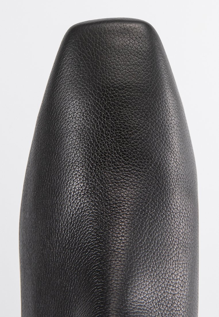 Zwarte leren schoenpunt met een vierkante vorm en een gestructureerd korrelpatroon tegen een effen lichte achtergrond.
