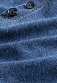 Sötétkék farmeranyag enyhén texturált felülettel, két fekete műanyag gombbal, kék díszítéssel.