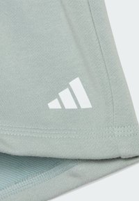 Il tessuto atletico verde chiaro presenta una texture liscia e un logo bianco ricamato con tre strisce parallele vicino all'orlo.