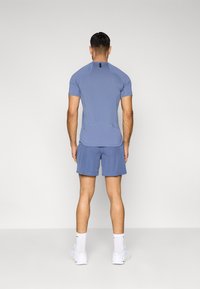 Ανοιχτό μπλε αθλητικό πουκάμισο με κοντά μανίκια, σετ με ταιριαστά σορτσάκια. Το ύφασμα φαίνεται λείο. Περιλαμβάνει μια μαύρη ετικέτα στο λαιμό.