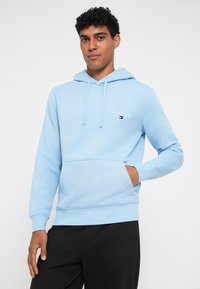 Φωτεινό μπλε φούτερ με καγκουρό τσέπη, κουκούλα με κορδόνι και κεντημένο λογότυπο μάρκας στο στήθος. Φτιαγμένο από απαλό ύφασμα από βαμβακερό μείγμα.