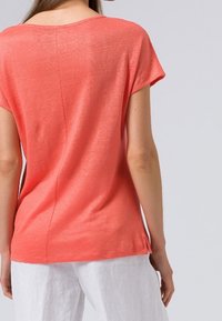 Korallfärgad kortärmad topp med rundad halsringning, slät textur och detalj med söm på baksidan, kombinerad med vita byxor.