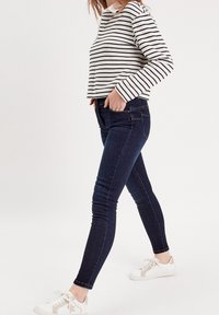 Jeans skinny bleu marine associés à un haut à rayures blanches et noires et des baskets blanches. La tenue présente un design décontracté et ajusté.