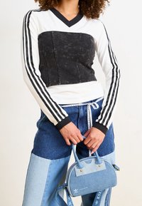 Czarny i biały longsleeve z krótkim krojem, w połączeniu z niebieskimi dżinsowymi spodniami w różnych odcieniach. Mała niebieska torebka na uchwytach.