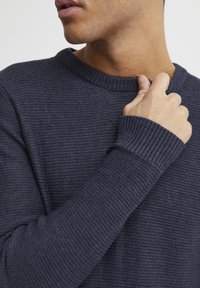 Pulover tricotat de culoare albastru închis, cu guler rotund cu nervuri și mâneci cu manșete, evidențiind un material texturat cu un model subtil.
