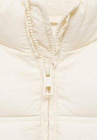 Cremfarbener Pufferjacke mit hohem Kragen, einem Reißverschluss mit quadratischem Ziehband und genähten Akzenten auf den Paneelen.