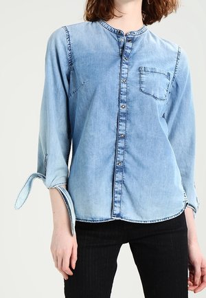 Light blue denim shirt with a band collar, front button closure, single chest pocket, and rolled-up sleeves. Smooth texture with faded details.