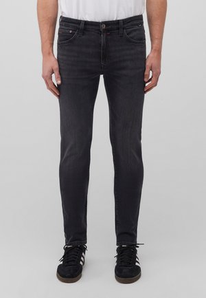 Black skinny jeans made of denim with a slight fade, five pockets, and a button closure. Worn with black lace-up sneakers.