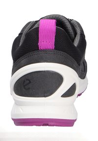 Scarpa sportiva nera con tomaia in mesh testurizzato, suola intermedia bianca e accenti viola sul tallone e sulla suola esterna. Presenta una linguetta per una calzata più facile.