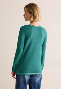 Tealstickad tröja med strukturerad yta, långa ärmar och rundad halsringning. Kombinerad med löst sittande blå denimjeans.