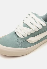 Light blue suede sneaker with white canvas accents and laces, featuring a textured rubber sole and stitched detailing.