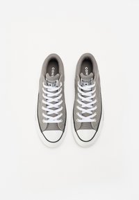 Sneakers alta in tela grigia con lacci bianchi, punta in gomma e dettagli neri. Presentano un logo "Converse All Star" sulla linguetta.