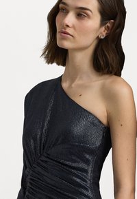 Asymmetrisk enskuld klänning i mörk metallisk tyg, med ruchingdetaljer och en slät silhuett, accentuerad av en mjuk textur.