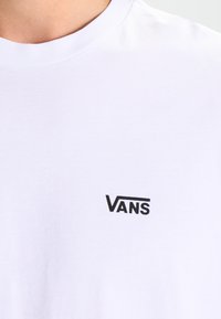 Vit bomull t-shirt med en svart Vans-logga på vänstra bröstet. Designen inkluderar en klassisk rund halsringning och en mjuk textur.