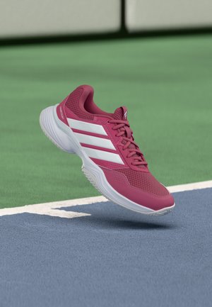 Chaussure de sport rouge et blanche flottant au-dessus de la surface verte et bleue d'un court de tennis près de la ligne blanche de délimitation.