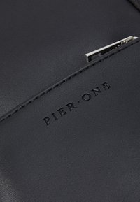 Black leather bag with embossed "PIER.ONE" logo, featuring a silver zipper and subtle stitching along the edge. Smooth texture.