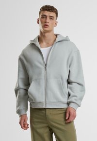 Hellgrau Zip-Hoodie mit geräumiger Kapuze, zwei Fronttaschen und gerippten Bündchen. Hergestellt aus einem weichen Baumwollmischgewebe.